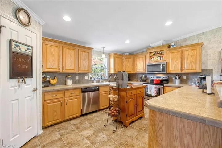 Kitchen with decorative light fixtures, decorative backsplash, ornamental molding, appliances with stainless steel finishes, and light tile patterned floors
