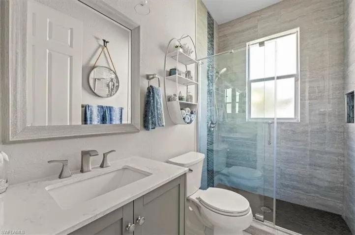 Bathroom featuring a shower with shower door, vanity, and toilet