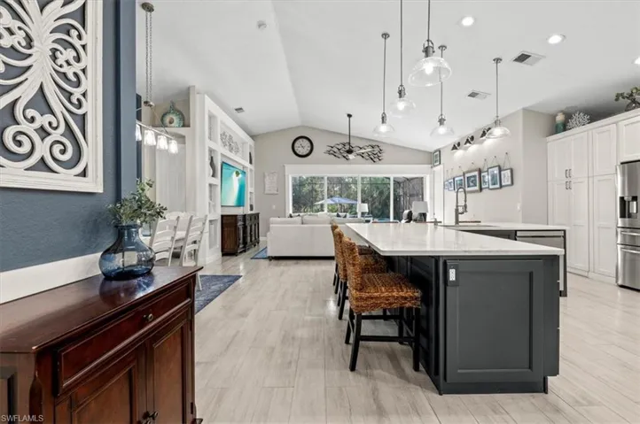 Kitchen featuring lofted ceiling, a breakfast bar, white cabinetry, light hardwood / wood-style flooring, and a large island with sink