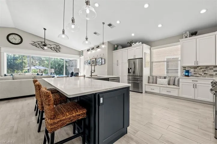 Kitchen with vaulted ceiling, white cabinets, sink, a large island with sink, and stainless steel fridge