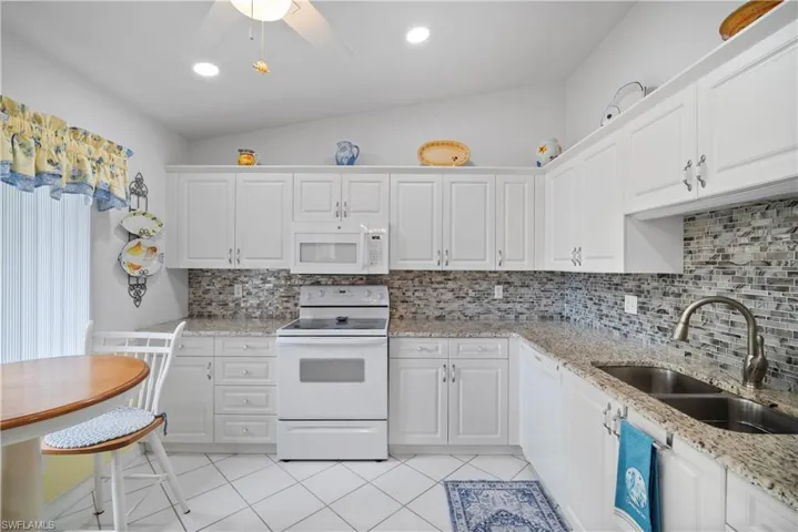 Kitchen featuring sink, vaulted ceiling, white cabinetry, white appliances, and tasteful backsplash