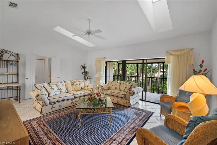 Tiled living room featuring ceiling fan, high vaulted ceiling, and a skylight