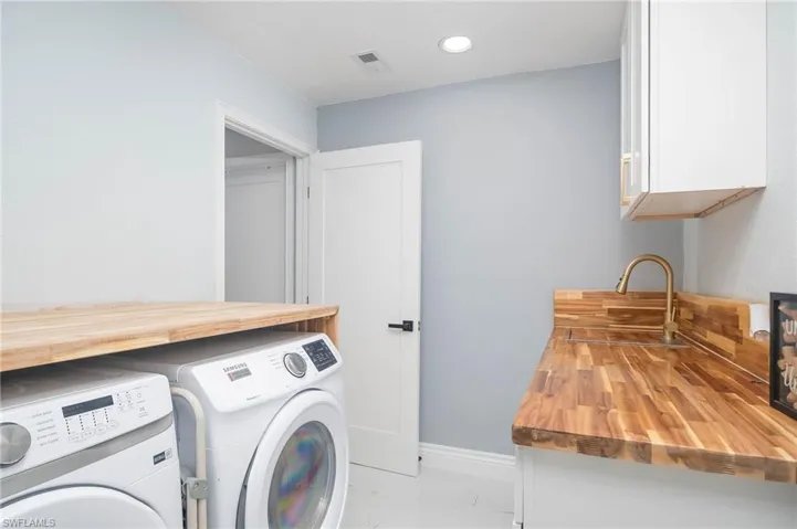 Clothes washing area featuring sink, washer and clothes dryer, and cabinets