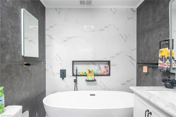 Bathroom with toilet, a tub, vanity, crown molding, and tile walls