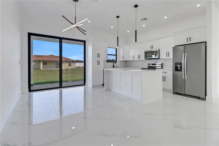Kitchen with appliances with stainless steel finishes, white cabinets, hanging light fixtures, and a kitchen island