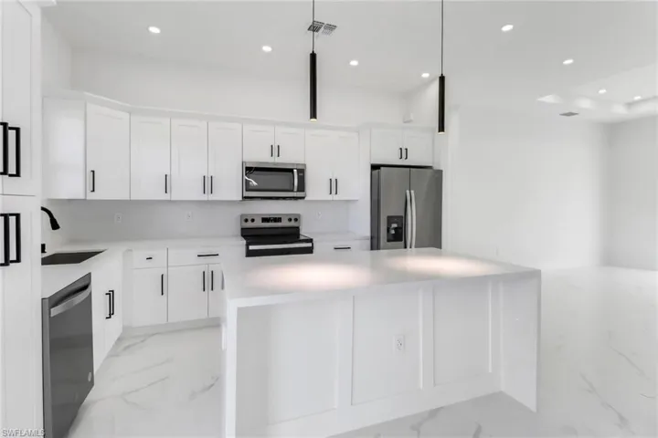 Kitchen featuring sink, a center island, hanging light fixtures, stainless steel appliances, and white cabinets