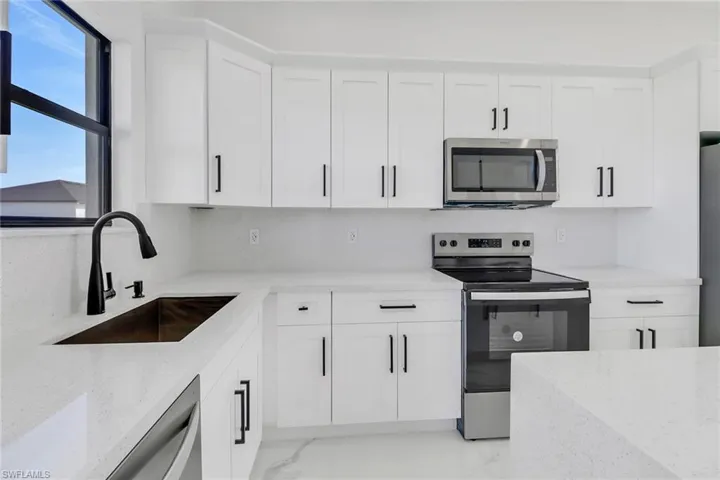 Kitchen with light stone countertops, sink, white cabinetry, and stainless steel appliances
