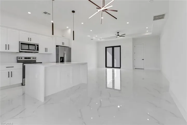 Kitchen with hanging light fixtures, stainless steel appliances, a center island, white cabinets, and ceiling fan