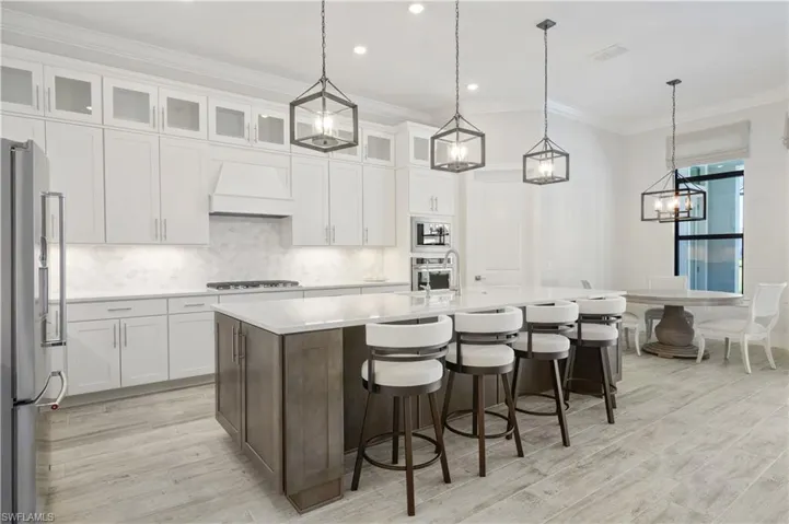 Kitchen with appliances with stainless steel finishes, light wood-style floors, premium range hood, tasteful backsplash, and crown molding