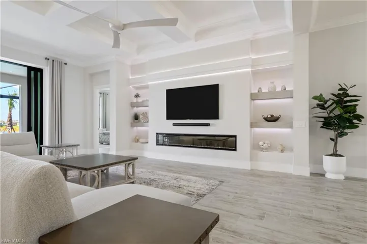 Living area featuring coffered ceiling, ornamental molding, a glass covered fireplace, beamed ceiling, and wood finished floors