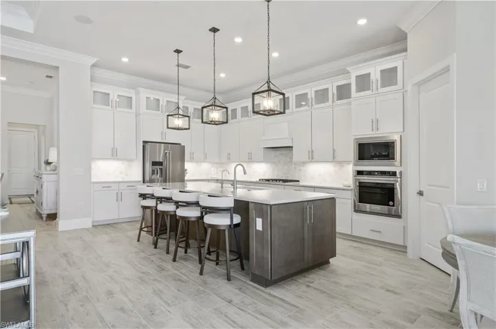 Kitchen featuring appliances with stainless steel finishes, a large island with sink, light countertops, white cabinets, and ornamental molding