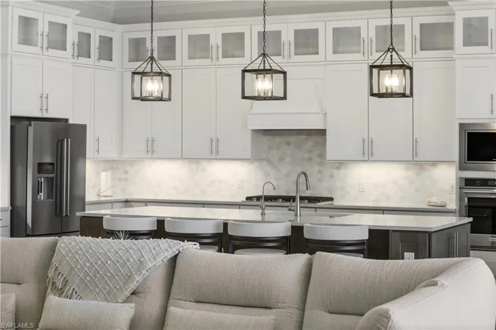 Kitchen featuring stainless steel appliances, light countertops, open floor plan, an island with sink, and a kitchen bar