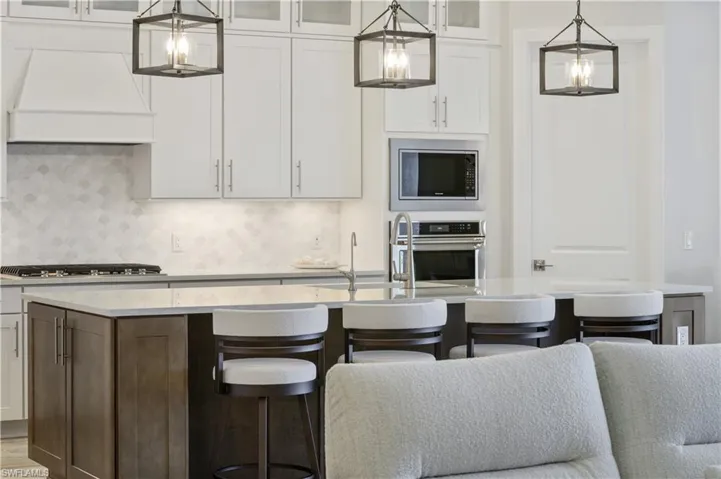 Kitchen with a center island with sink, premium range hood, a breakfast bar, stainless steel appliances, and glass insert cabinets