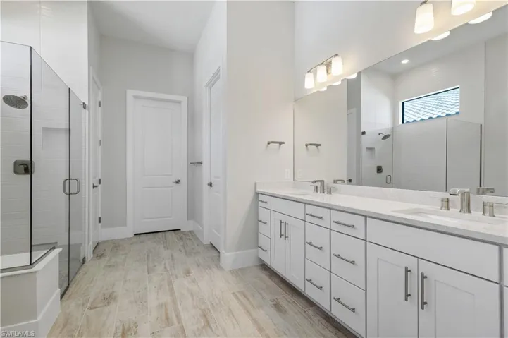 Bathroom featuring a stall shower, double vanity, wood finished floors, and recessed lighting