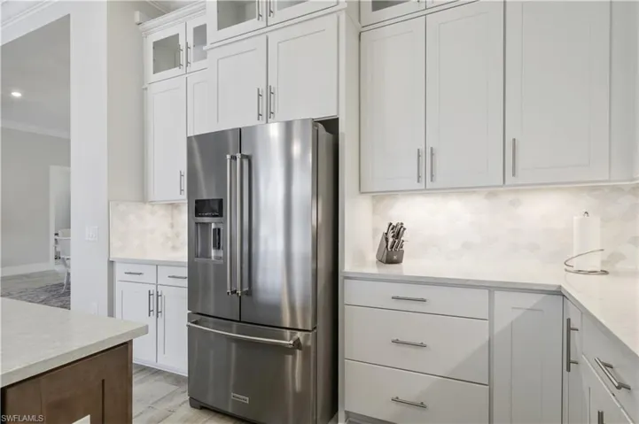 Kitchen featuring high end refrigerator, ornamental molding, decorative backsplash, white cabinets, and light wood-style floors