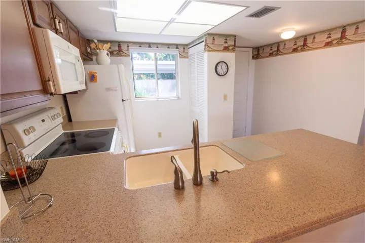 Kitchen featuring white appliances, light stone counters, a peninsula, and brown cabinets