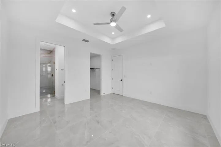 Unfurnished bedroom with a tray ceiling, a walk in closet, ceiling fan, recessed lighting, and connected bathroom