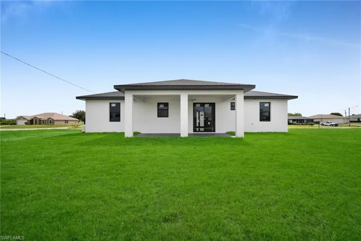 Back of property featuring a yard, stucco siding, and roof with shingles