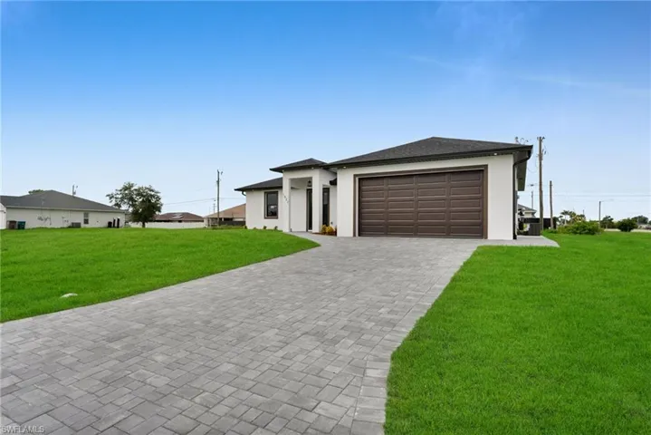Prairie-style home featuring a front yard, stucco siding, decorative driveway, and an attached garage
