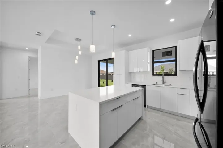 Kitchen with white cabinets, hanging light fixtures, recessed lighting, freestanding refrigerator, and modern cabinets