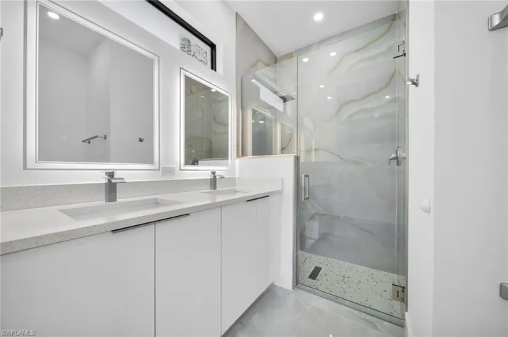 Bathroom featuring a marble finish shower, double vanity, light tile patterned floors, and recessed lighting