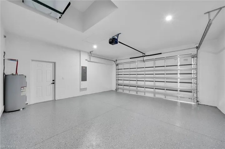 Garage with electric water heater, electric panel, and a garage door opener