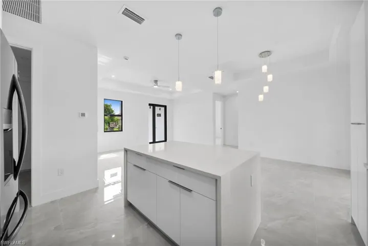 Kitchen with modern cabinets, a raised ceiling, white cabinetry, hanging light fixtures, and stainless steel fridge with ice dispenser