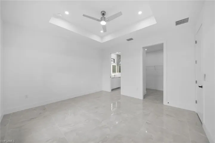 Unfurnished bedroom featuring a tray ceiling, a spacious closet, a ceiling fan, recessed lighting, and connected bathroom