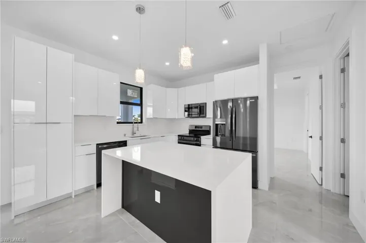 Kitchen with modern cabinets, white cabinetry, appliances with stainless steel finishes, decorative light fixtures, and a center island