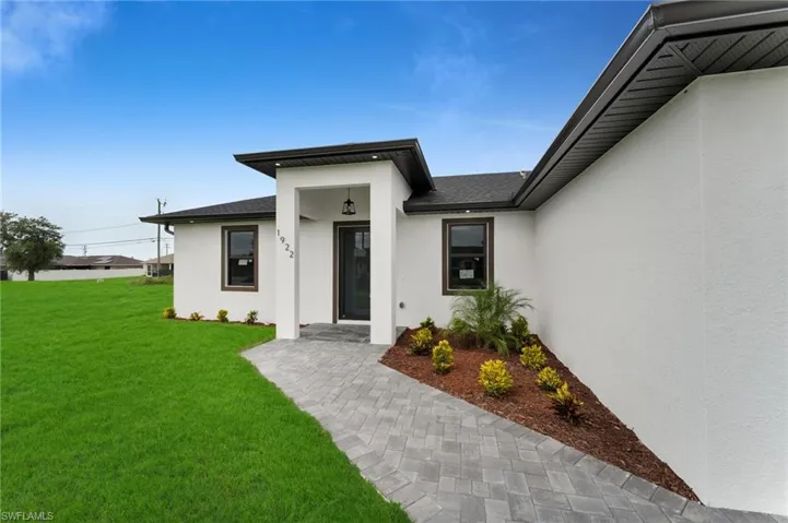 Property entrance with stucco siding, a yard, and roof with shingles