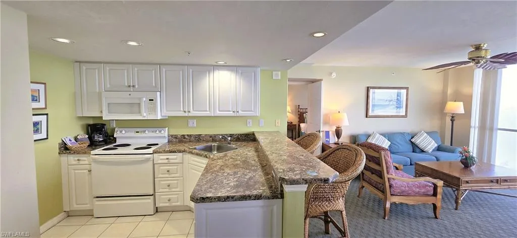 Kitchen with a breakfast bar, white appliances, white cabinetry, open floor plan