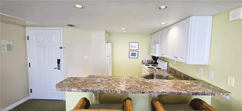Kitchen with a breakfast bar area, white cabinetry, white appliances, and recessed lighting