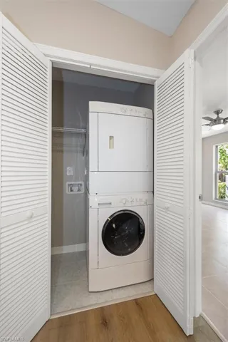 Washroom featuring ceiling fan, light wood-style floors, and stacked washer / dryer