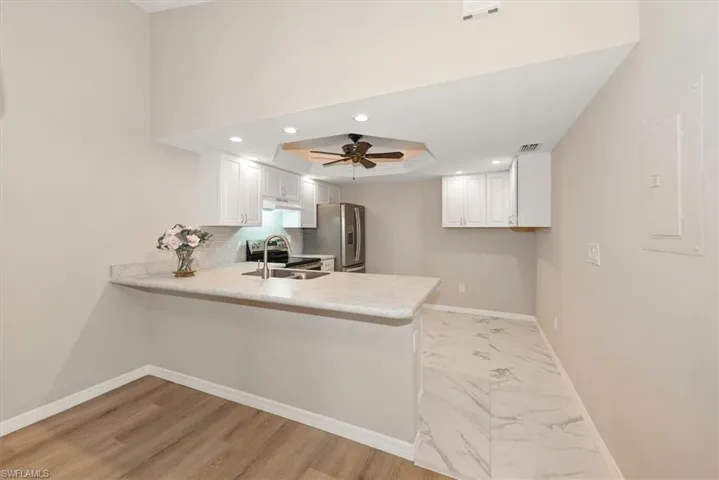 Kitchen featuring recessed lighting, light countertops, a peninsula, a tray ceiling, and electric panel