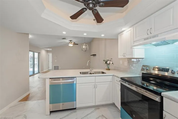Kitchen featuring stainless steel appliances, light marble finish flooring, decorative backsplash, under cabinet range hood, and white cabinetry