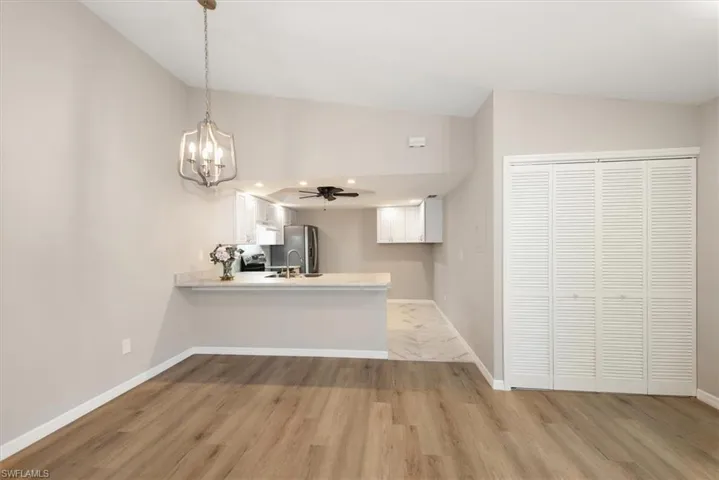 Kitchen with white cabinetry, a peninsula, a chandelier, light wood-style floors, and stainless steel fridge