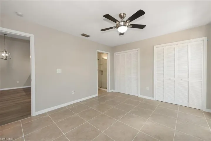 Unfurnished bedroom featuring light tile patterned floors, multiple closets, a ceiling fan, and a chandelier