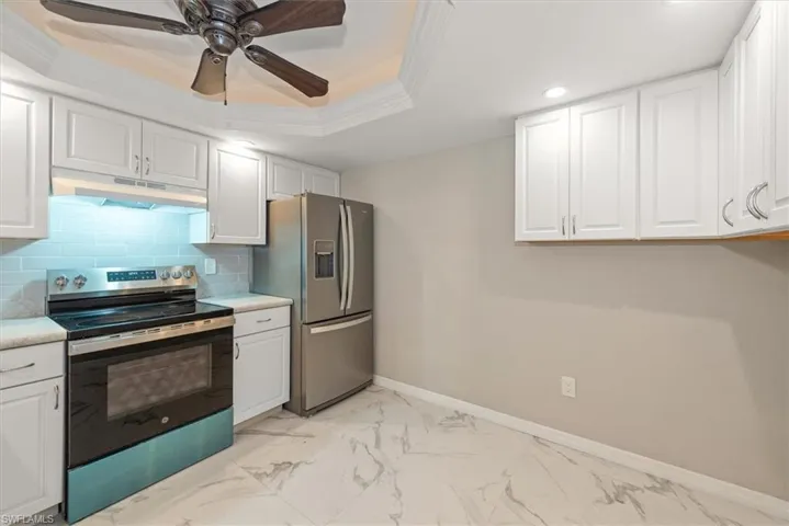 Kitchen featuring stainless steel appliances, white cabinetry, a tray ceiling, light marble finish flooring, and decorative backsplash