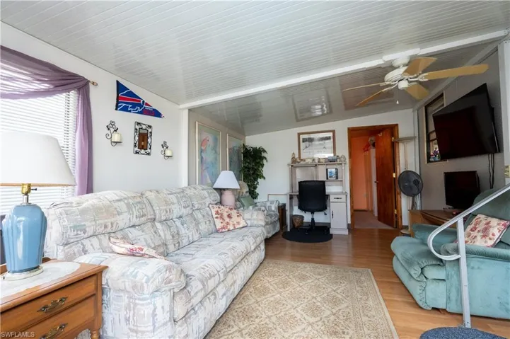 Living area featuring wood-finish flooring, a white paneled ceiling, and a ceiling fan with light fixture