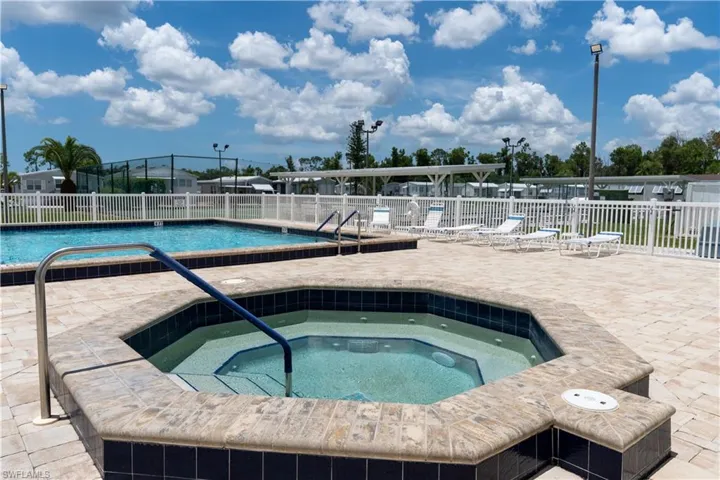 Octagonal spa with tiled surfacing, surrounded by a paved patio, swimming pool, and white fencing
