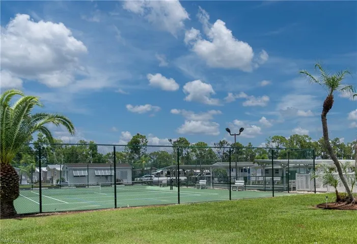 Tennis court with a green playing surface, perimeter fencing, and overhead lighting fixtures