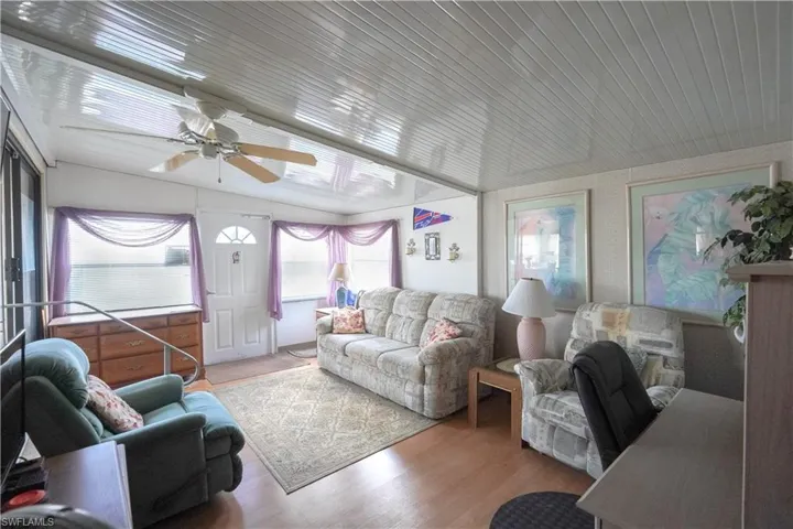 Living area featuring wood-finish flooring, a white paneled ceiling, and a ceiling fan with light fixture