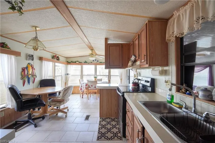 Kitchen and dining area featuring wood-finish cabinetry, tile flooring, and a semi-vaulted ceiling with exposed beam trim