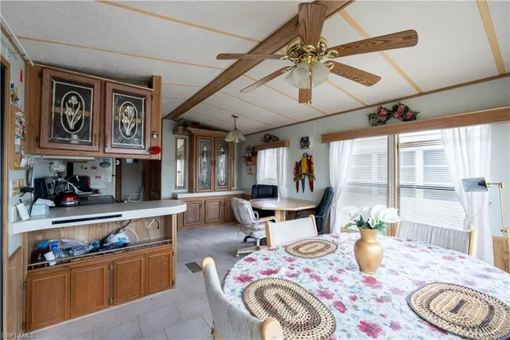 Dining area featuring wood-finish cabinetry, a ceiling fan with light fixture, and multiple windows with blinds