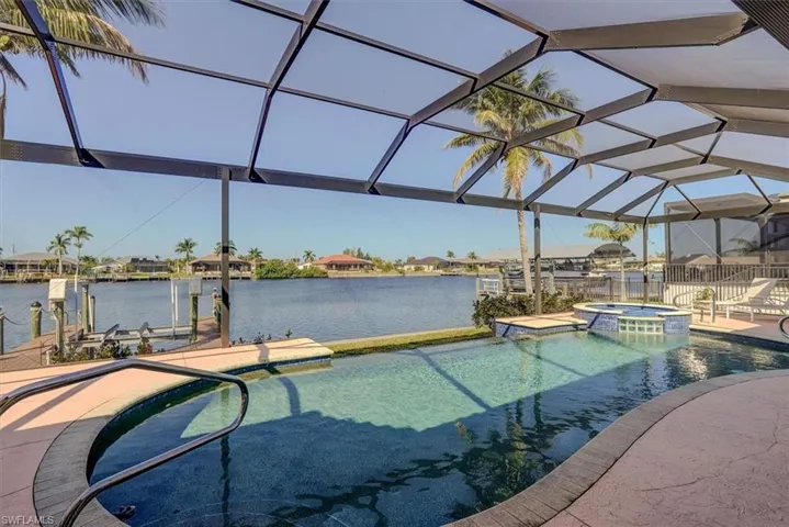 View of swimming pool with glass enclosure, a dock, a water view, a patio, and a pool with connected hot tub