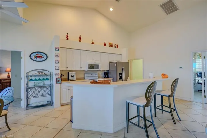 Kitchen with high vaulted ceiling, light tile patterned flooring, white appliances, white cabinets, and visible vents