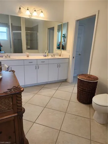 Full bath with a sink, toilet, a shower stall, double vanity, and tile patterned floors