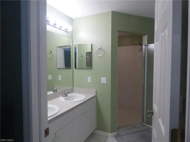 Bathroom featuring dual bowl vanity, a tile shower, and tile floors