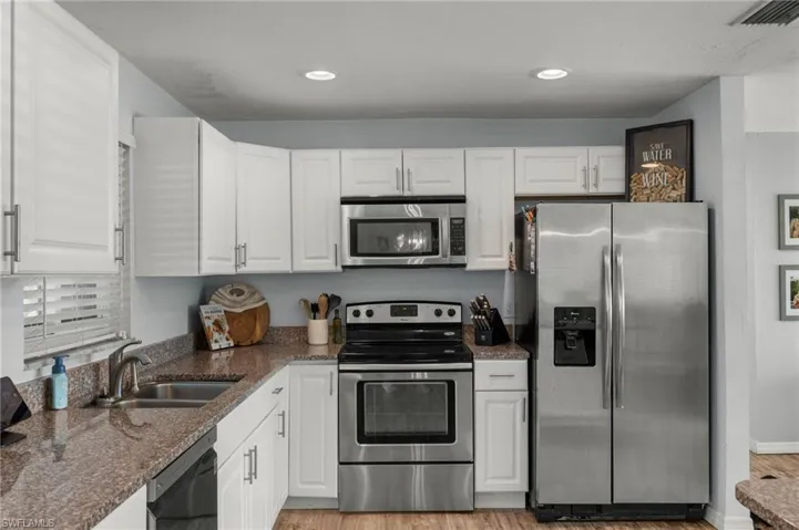 Kitchen with appliances with stainless steel finishes, white cabinetry, sink, dark stone countertops, and light wood-type flooring