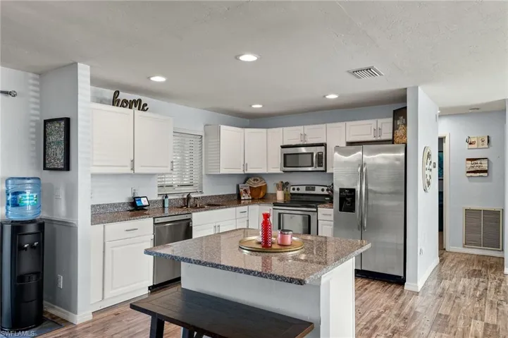 Kitchen with dark stone countertops, white cabinets, a center island, stainless steel appliances, and light wood-type flooring